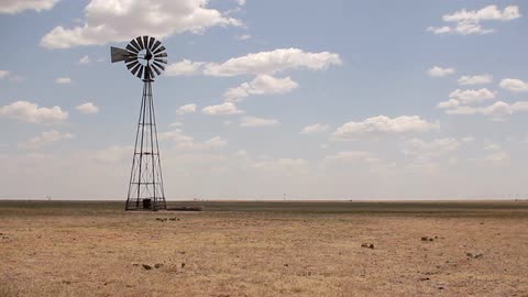 A windmill turns slowly in an open field