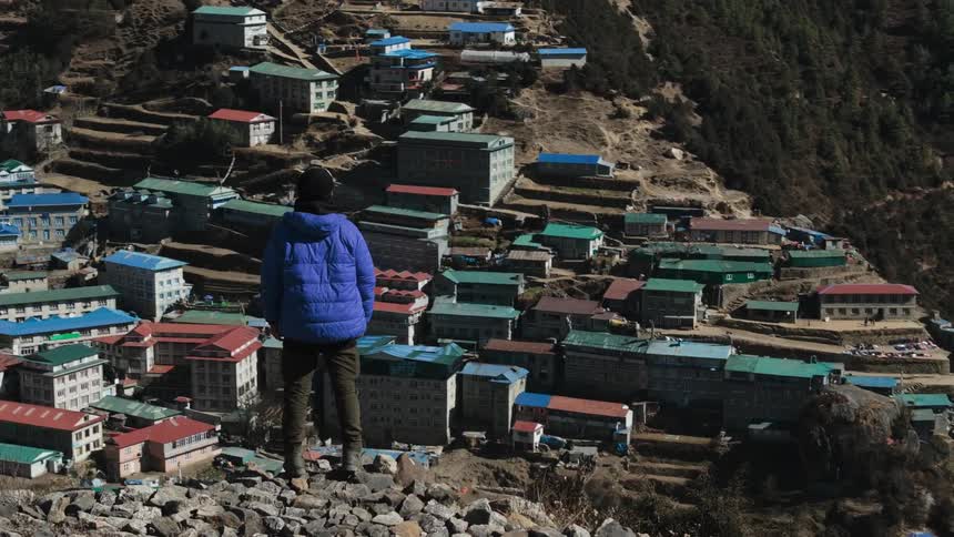 A male hiker stands on a ridge overlooking a valley filled with buildings