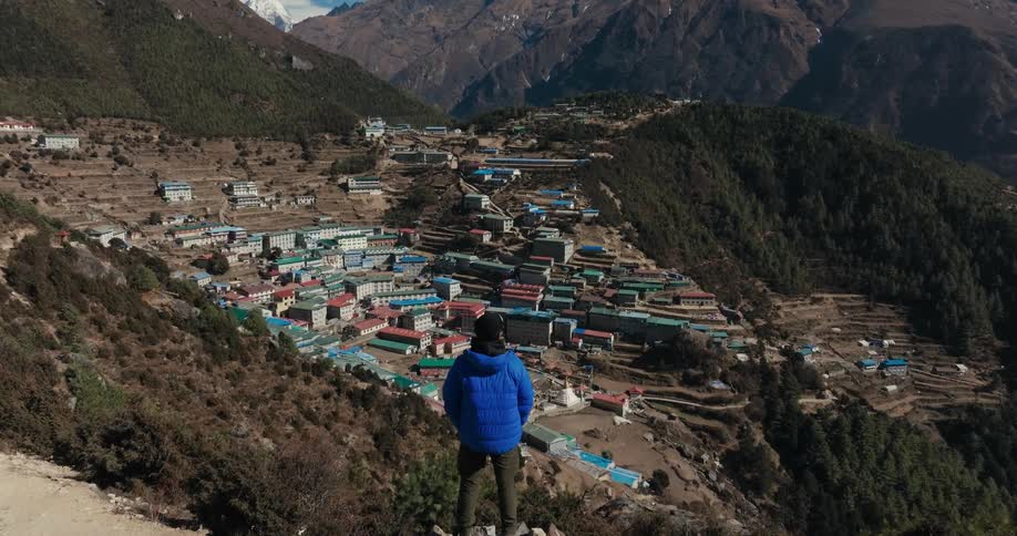 A person stands on a mountain overlooking a small rural town