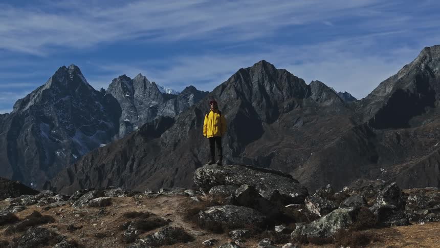 A hiker in a brightly colored jacket stands atop a mountain ridge