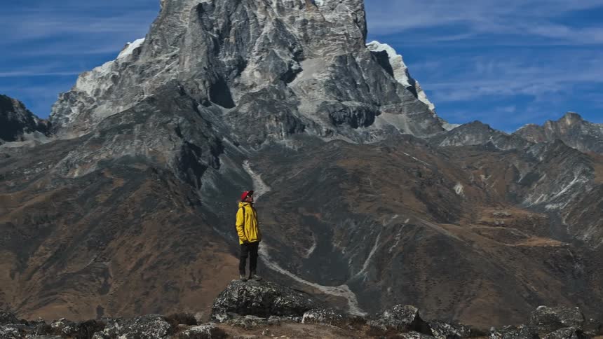 A man stands on a rock and looks at the mountainous terrain around him