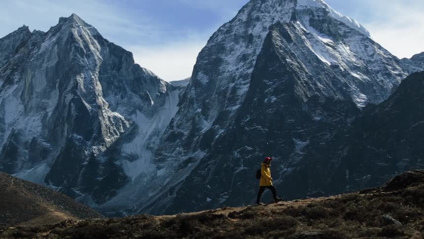 A man wearing a yellow coat and a black backpack hikes up a mountain as dusk sets in