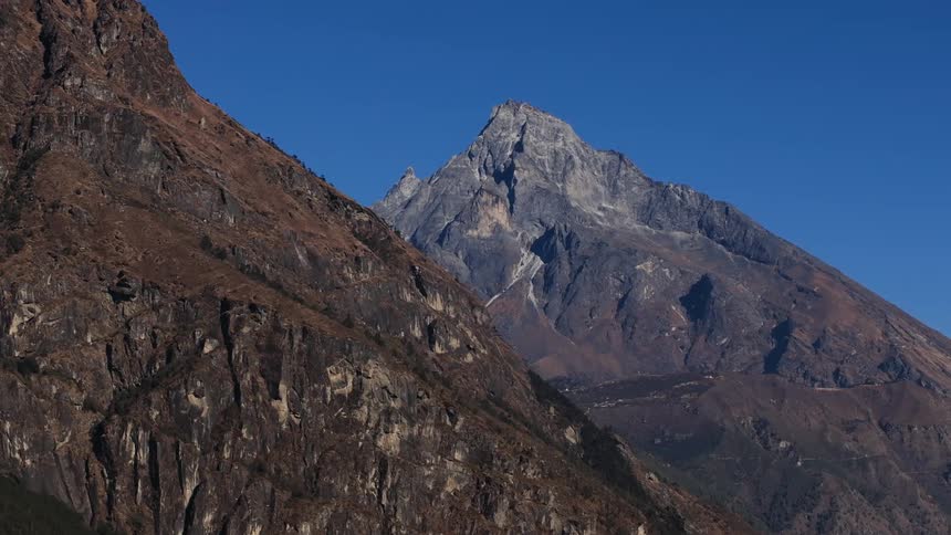 A towering rocky mountain stands tall under a clear blue sky