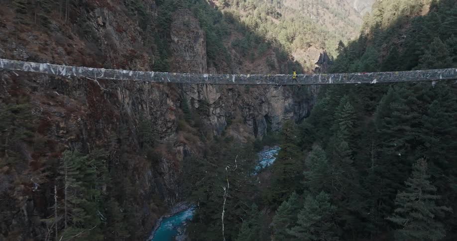 A man walks across a suspension bridge over a river