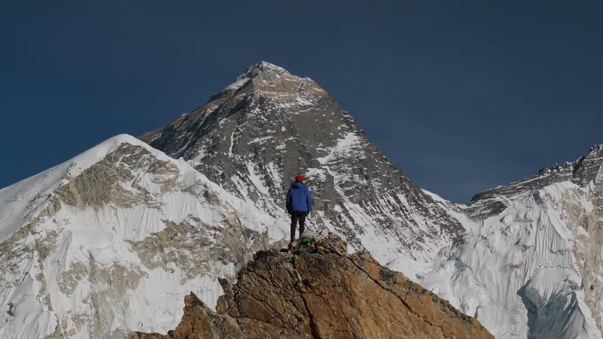 A person at the very peak of a mountain gazing at the snowy mountain range in front of them