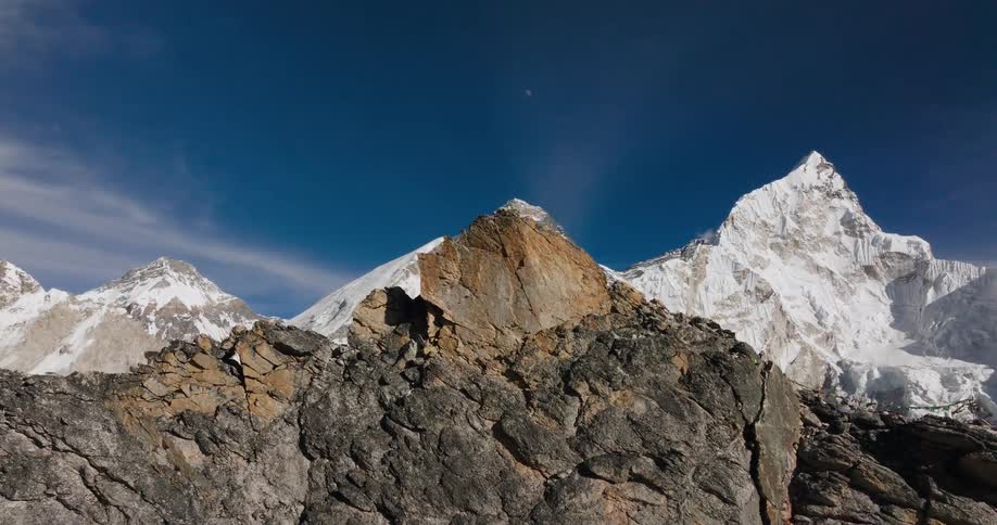 The peak of a rocky mountain and behind it is a huge mountain covered in snow