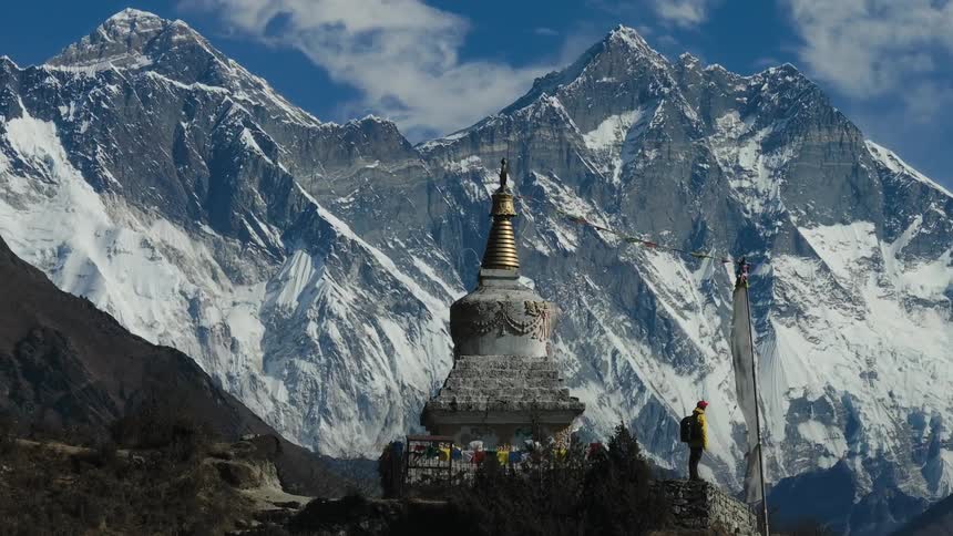 Man on a cliff side long surrounded by mountain ranges covered by snow