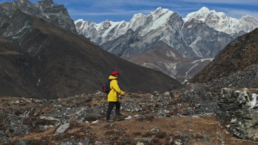 Man walking on a hill with rocks and mountains with snow around him