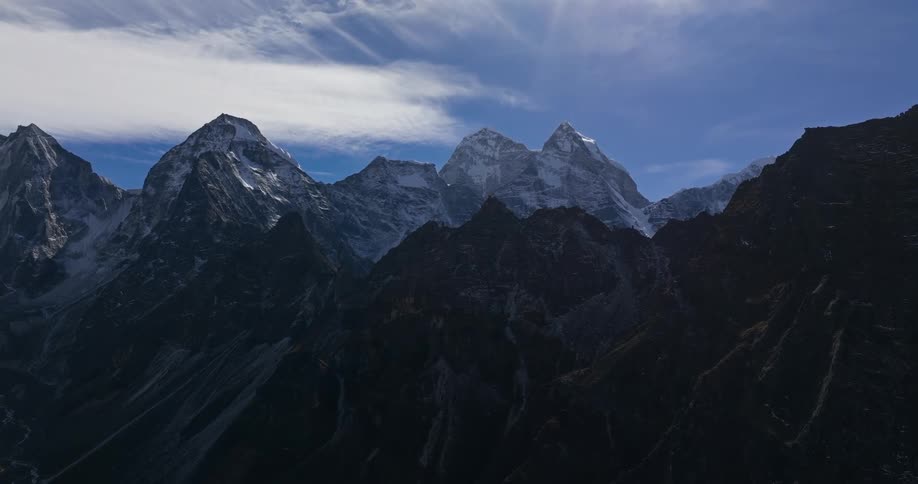 A rocky mountain range is coated with snow under a partially cloudy sky
