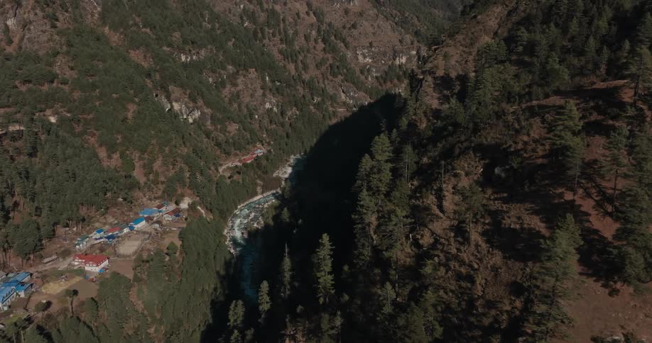 A valley between two mountains where there is a stream and many trees on the sides