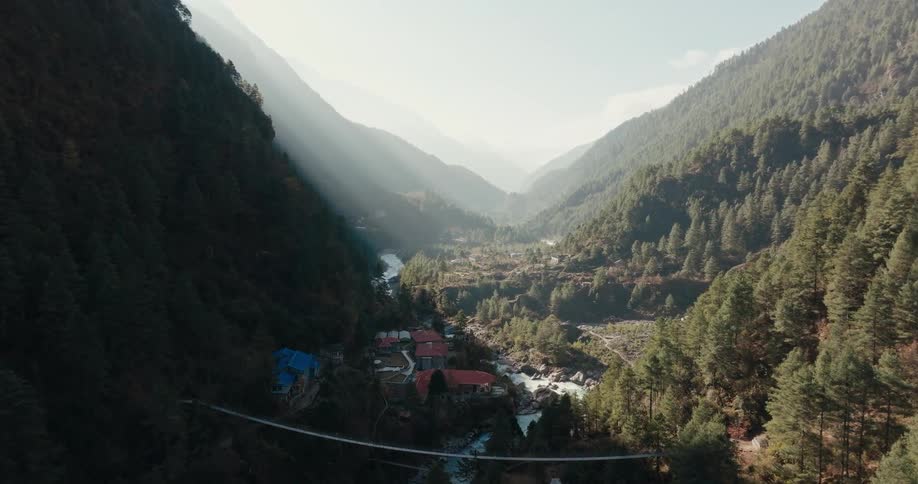 A small community is located in a forested valley located between towering mountains