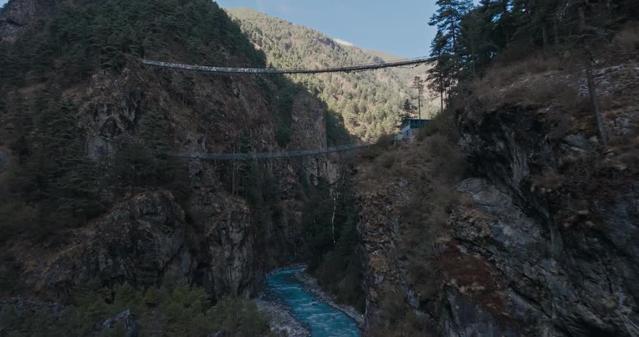 Aerial of a suspension bridge over a river in a mountainous valley