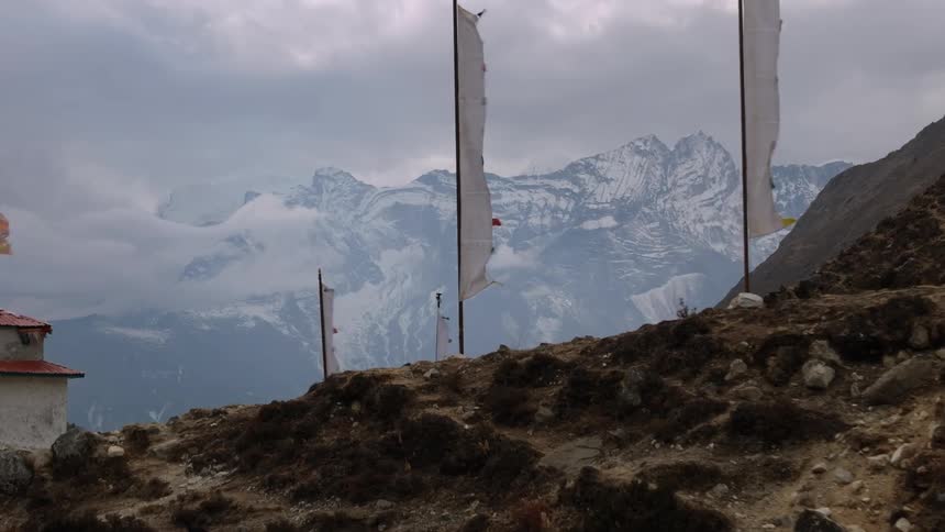 Sanctuary and flags on a hill surrounded by mountains covered in snow on a cloudy day