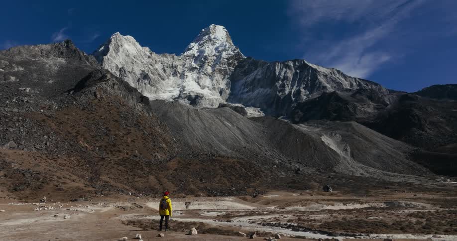 A lone hiker stands in a valley while looking up at the surrounding mountain range