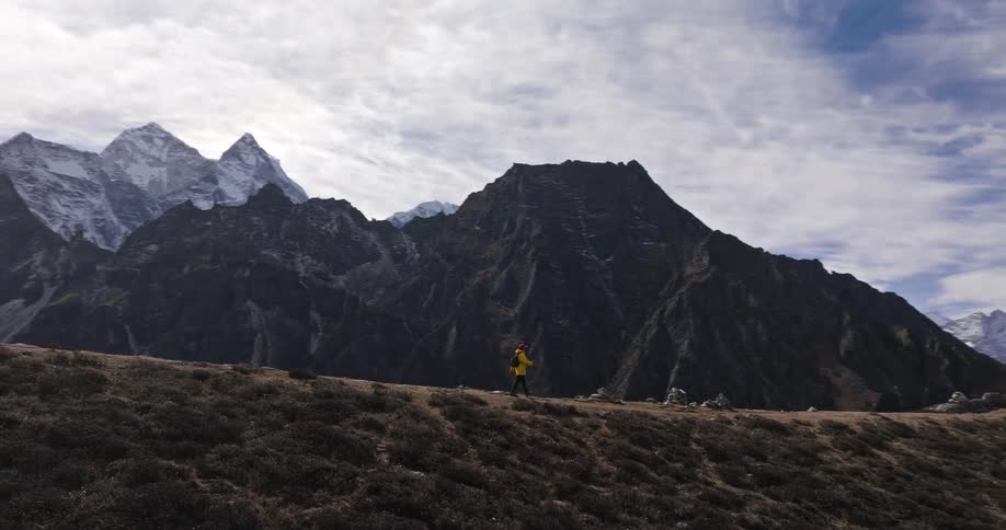 A person in a yellow jacket walking along a path surrounded by huge mountains
