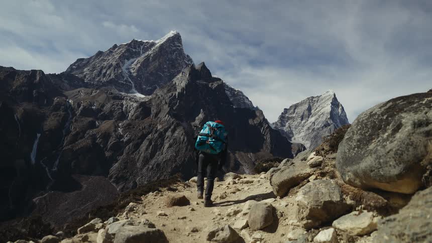 A hiker traverses rough terrain with mountains in the background