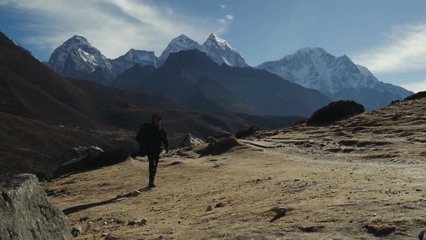 A lone hiker wearing a backpack walk through a mountainlined valley