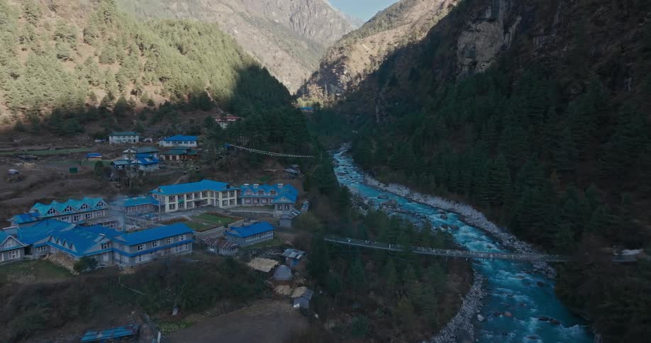 Aerial of buildings with blue roofing located on a hill at waterfront during the day