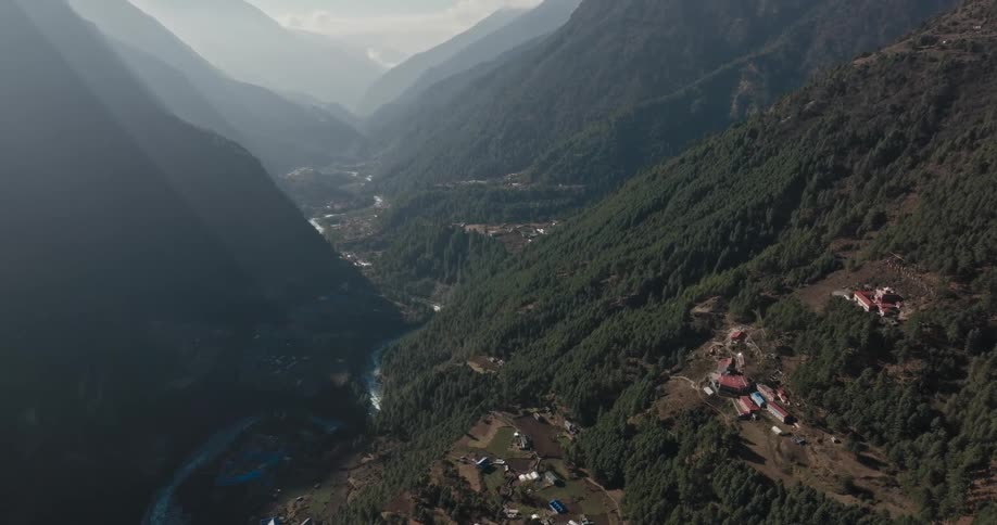 Aerial panorama of a village in the middle of mountains next to a river with solar reflection during the day