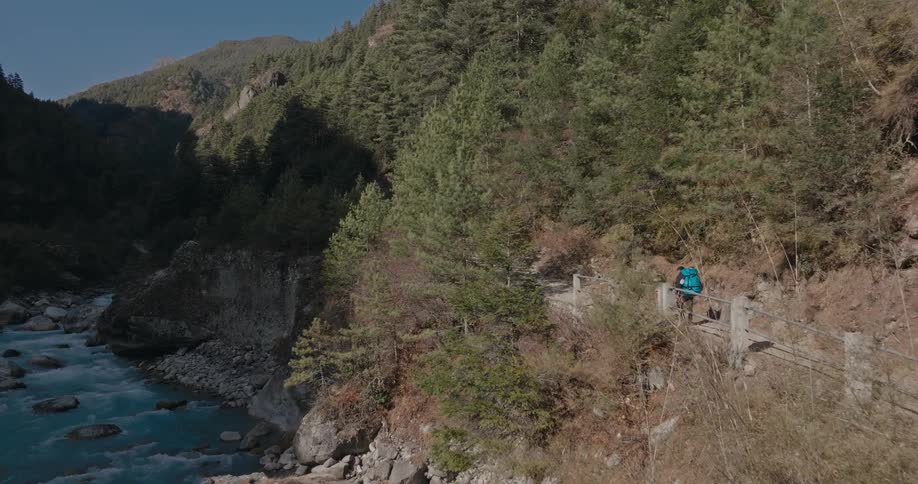 A lone hiker wearing a large backpack make his way along a river trail
