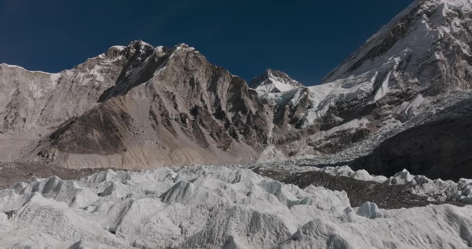 A huge mountain that on the ground there are small white elevations and on the top of the mountain there is snow
