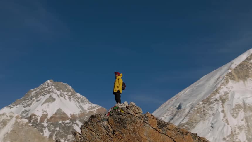 A man in a yellow jacket stands on the summit of a mountain