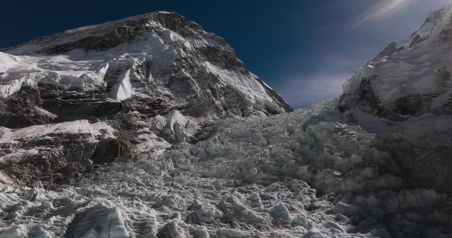 Landscape of rocky mountains with cliffs covered by snow on a dark blue sky day with sun flare