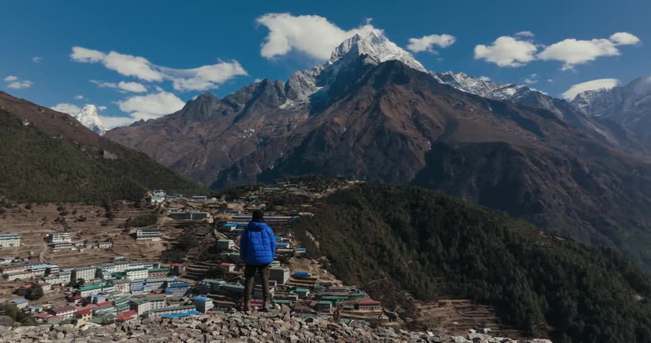 Man on a cliff observing the view of a village over mountains