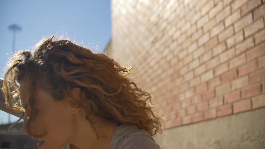 A woman dances in front of a brick wall in the sunshine
