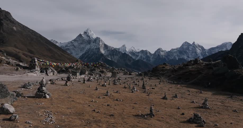 Religious cemetery with small stones piled up next to snowy mountains on a cloudy day