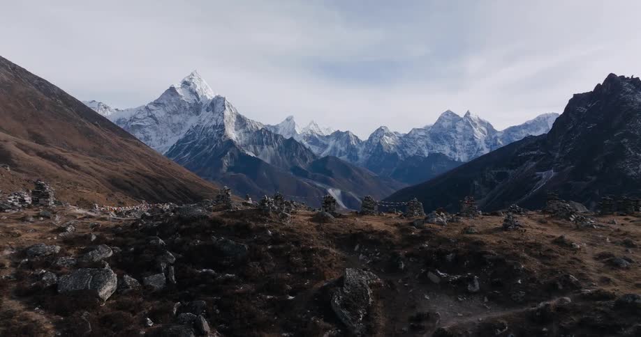 The top of a small mountain covered in rocks and in the background huge mountains with a top covered in snow