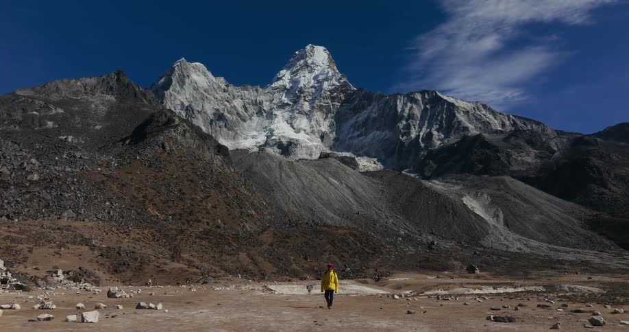 Man walking on a desert floor surrounded by mountain ranges covered by snow in daylight
