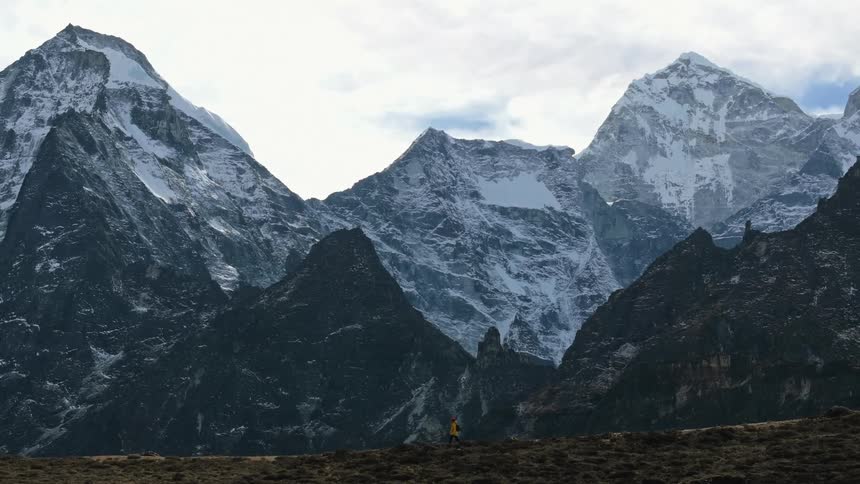 Person hiking on a hill surrounded by snowcovered mountain ranges on a cloudy day