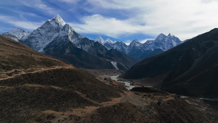 A valley with a small river that is between mountains and there is snow on top of them