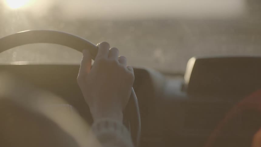 The sun shines brightly as a woman drives along a road