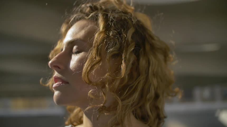 The wind blows a woman's hair as she stands with eyes closed in the sunshine