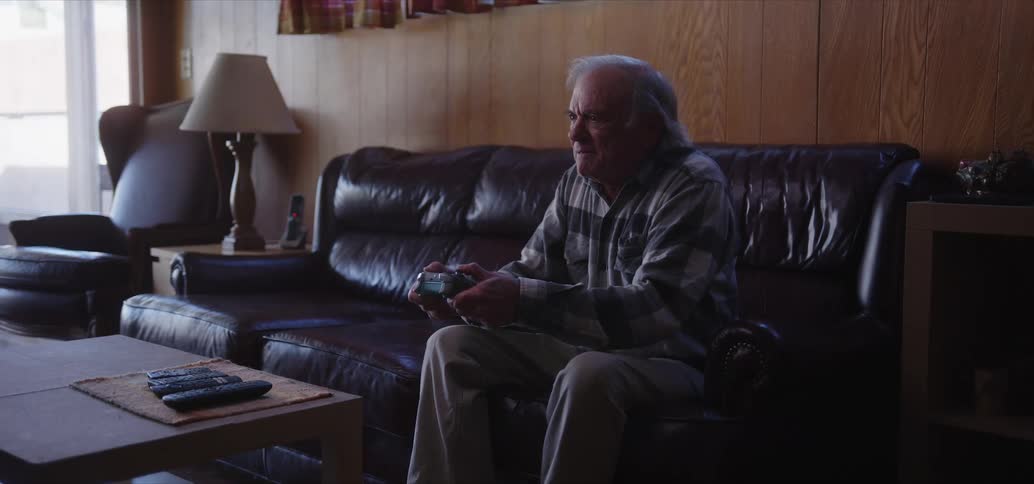 Elderly man sitting on the sofa in the living room holding a video game controller and having fun
