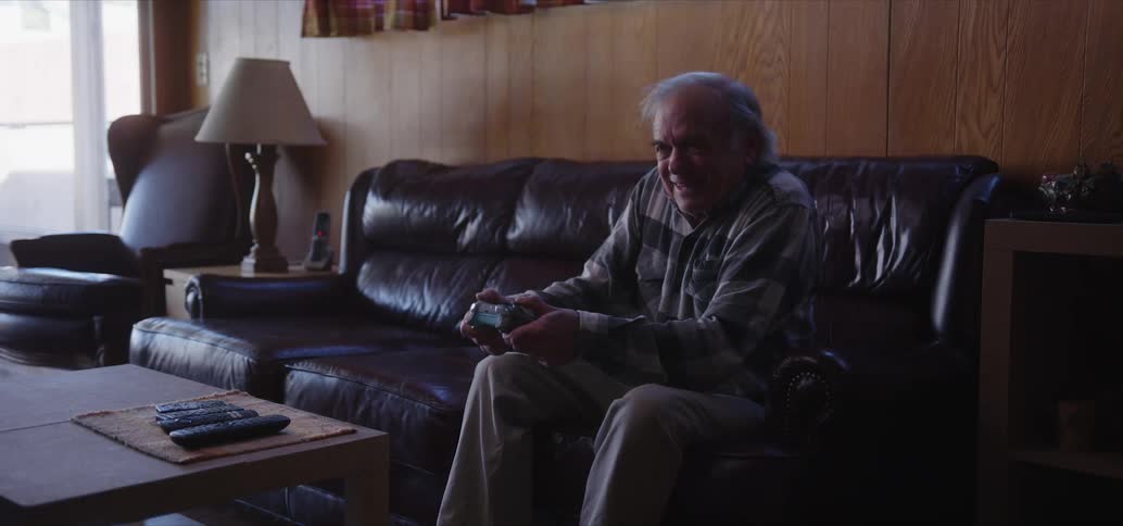 Elderly man wearing a plaid shirt and brown pants plays video games