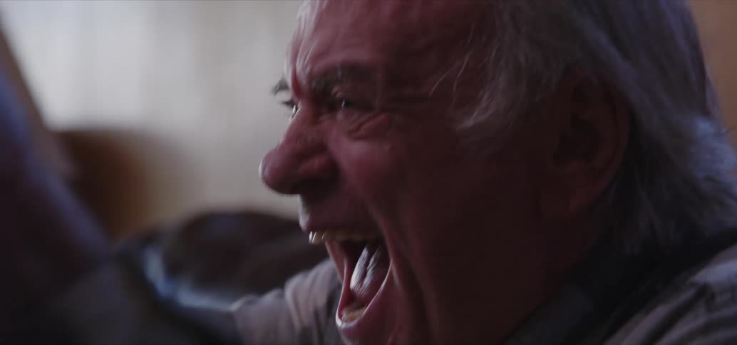 An old man sitting on the couch laughs and celebrates