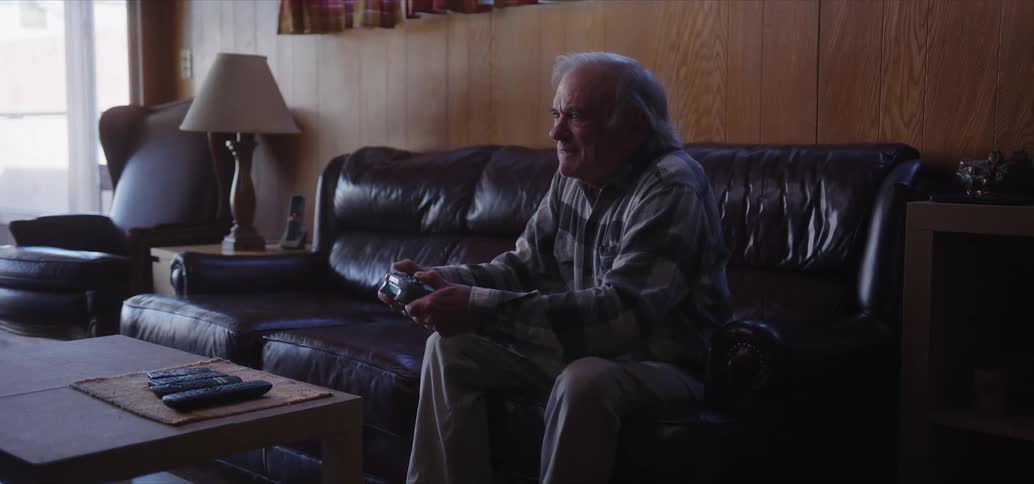 Older man sitting on living room couch manipulates game controller