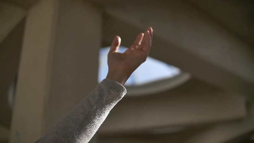 A person raising their hand up towards the sunlight near a bridge