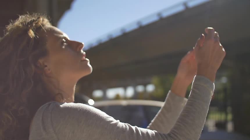 Woman holding her arms up and looking up at the sun under a bridge