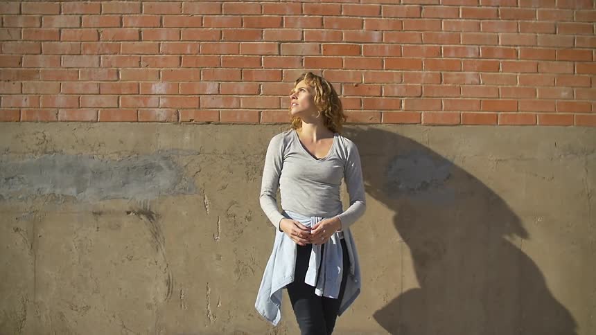 A woman stands next to a brick building on a sunny day