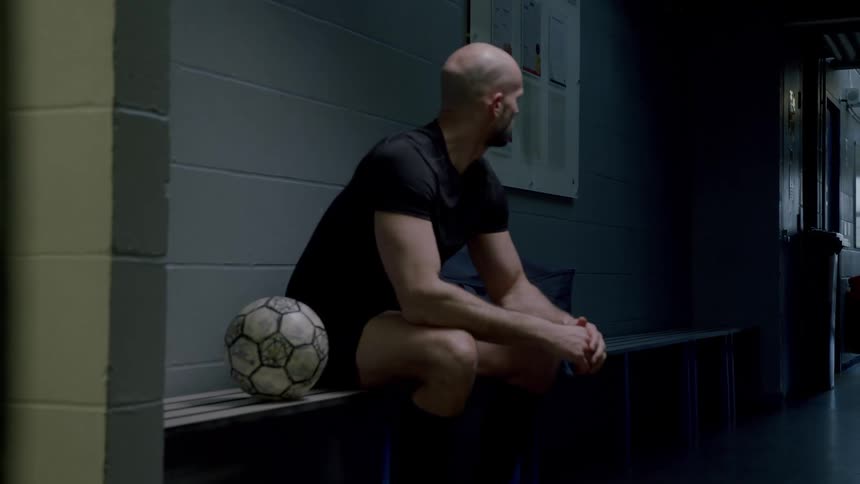 Man sitting in a locker room and next to him a soccer ball