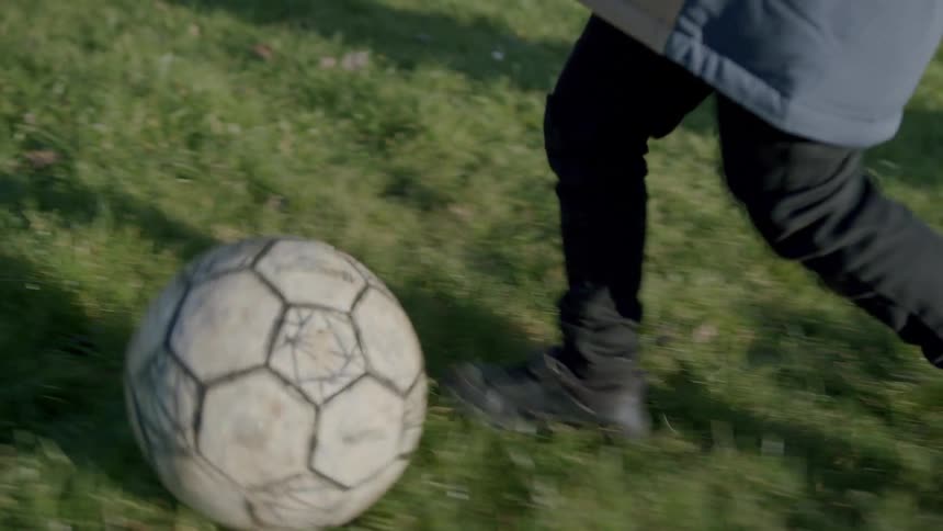 Close over the legs of a child running on a lawn with the soccer ball