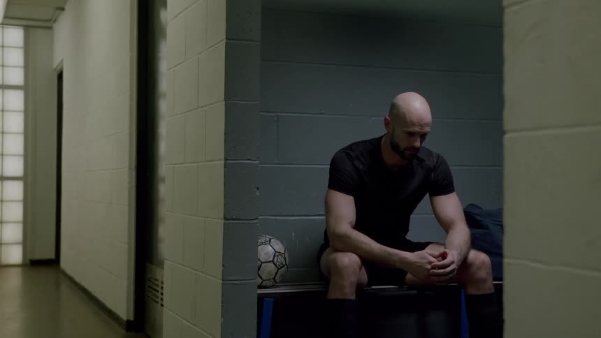 A man sits on a bench next to a soccer ball