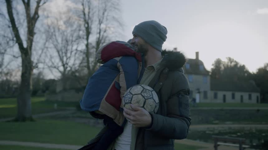 A father is holding his son and a soccer ball