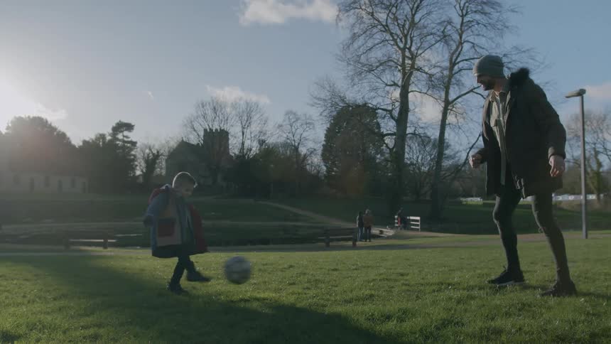 Father with his son on a lawn in a park touching the ball to each other with football passes