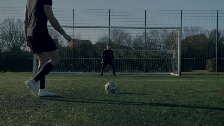 A man puts the ball down for a penalty kick while the goalkeeper awaits the kick