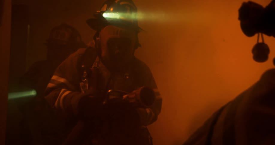 Three firefighters carry a hose down a hallway